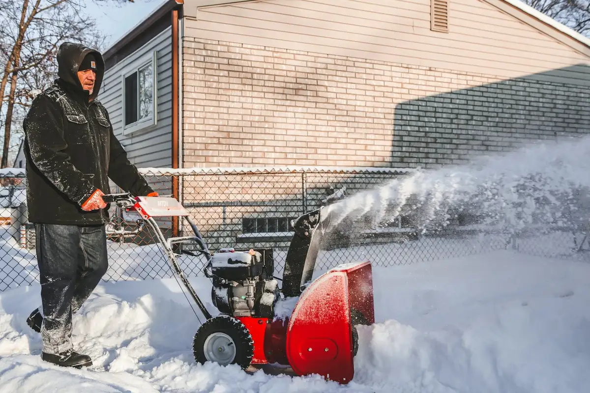 Snow blower clearing a driveway beside a house